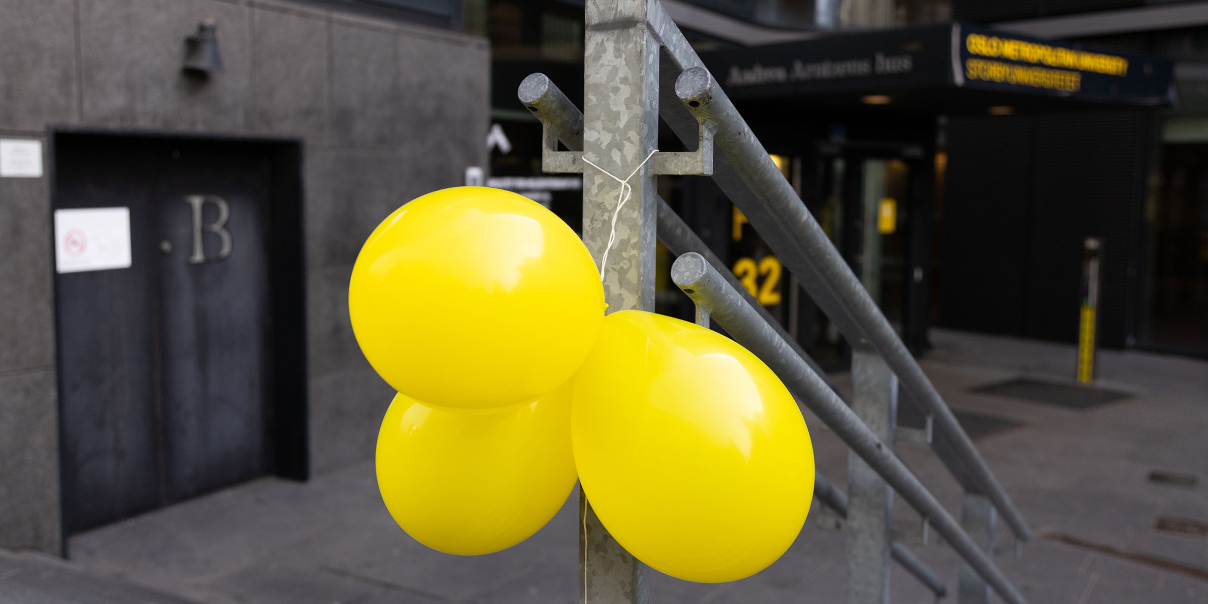 Tre gule ballonger som henger på gelenderet foran inngangen til Pilestredet 32.