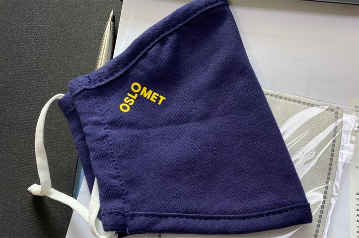 Bilde av mørkeblått stoff-munnbind med OsloMet-logo.