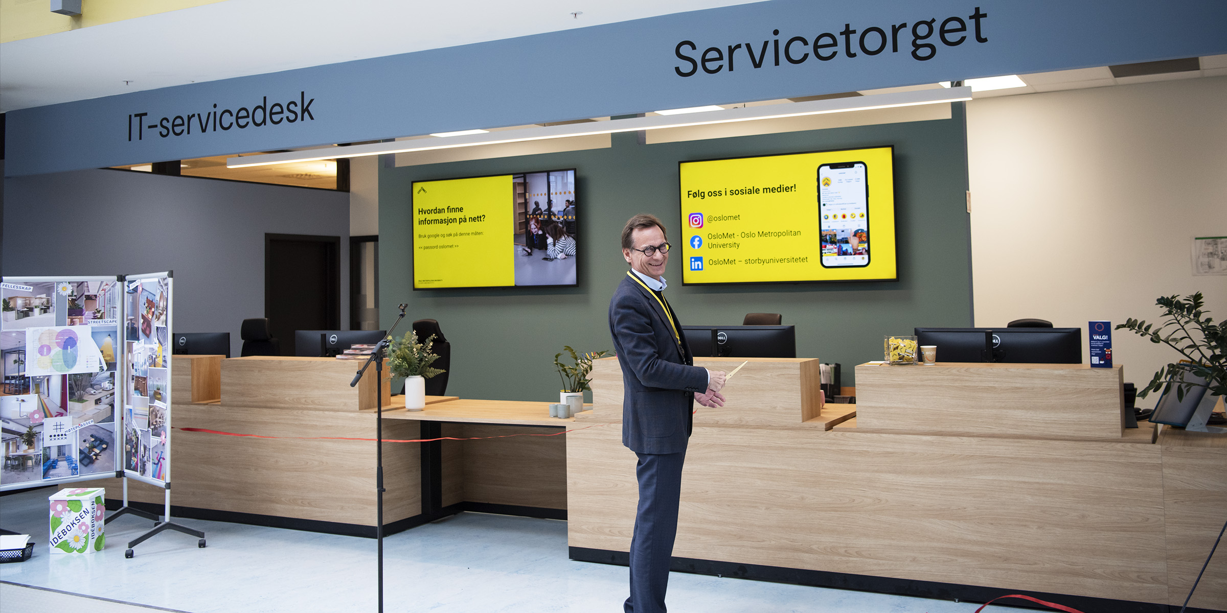 Foto av smilende rektor som står foran det nye servicetorget på Kjeller og har klippet båndet.