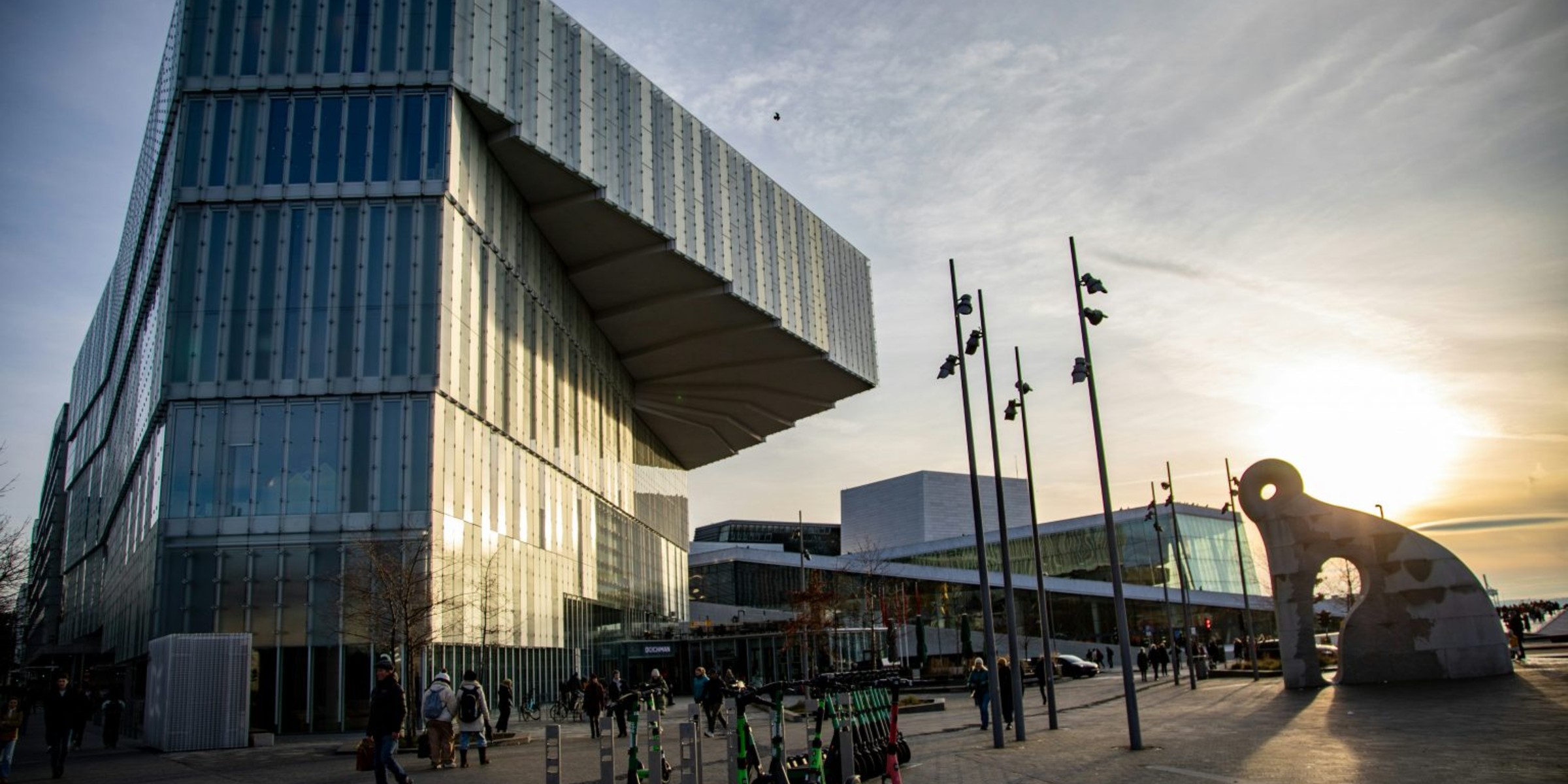 Foto av Deichman-bygget tatt utenfra med mennesker som går forbi.