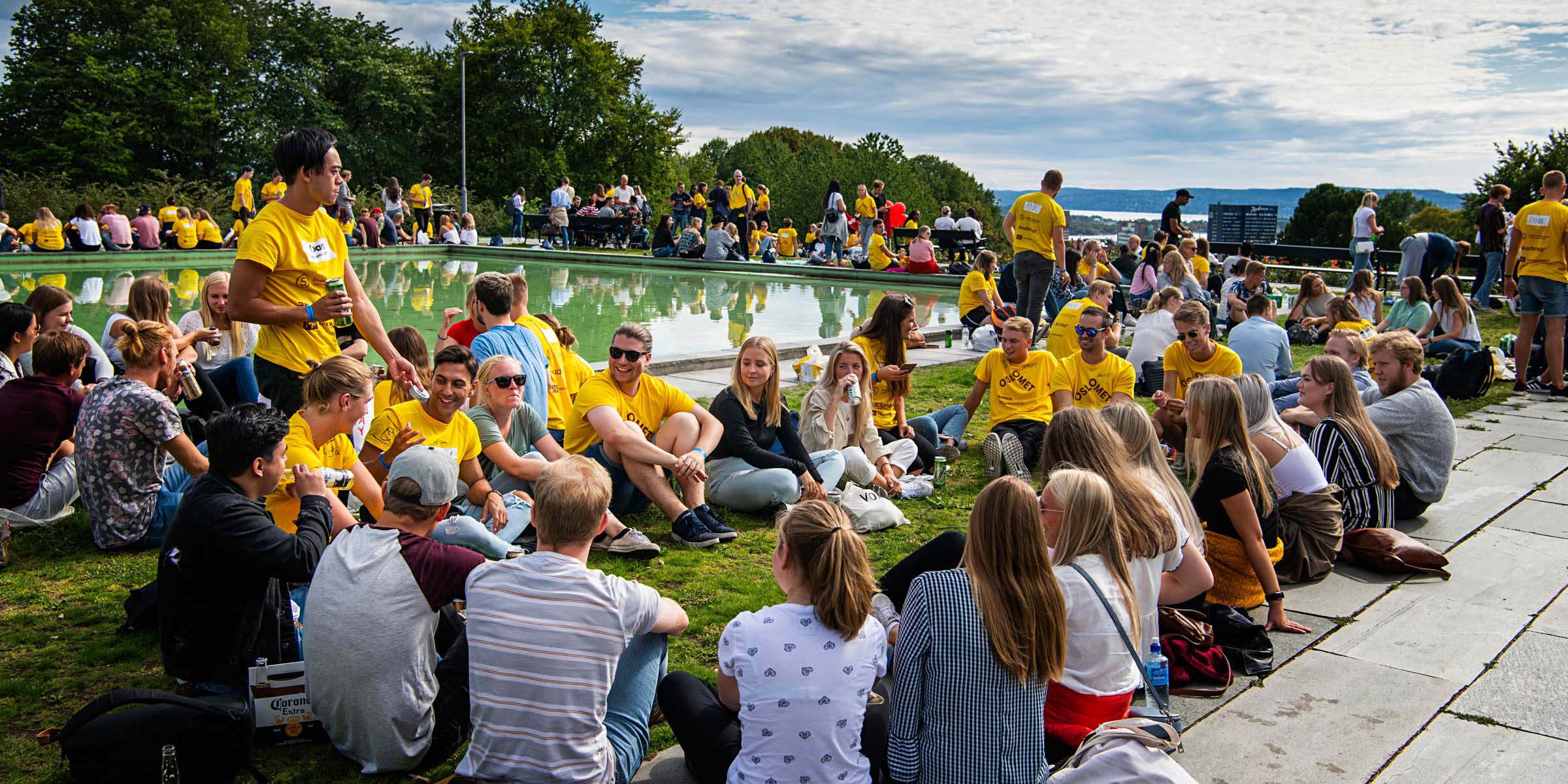 Mange studenter sitter på gresset i grupper under OsloMets åpningsseremoni på St.Hanshaugen.