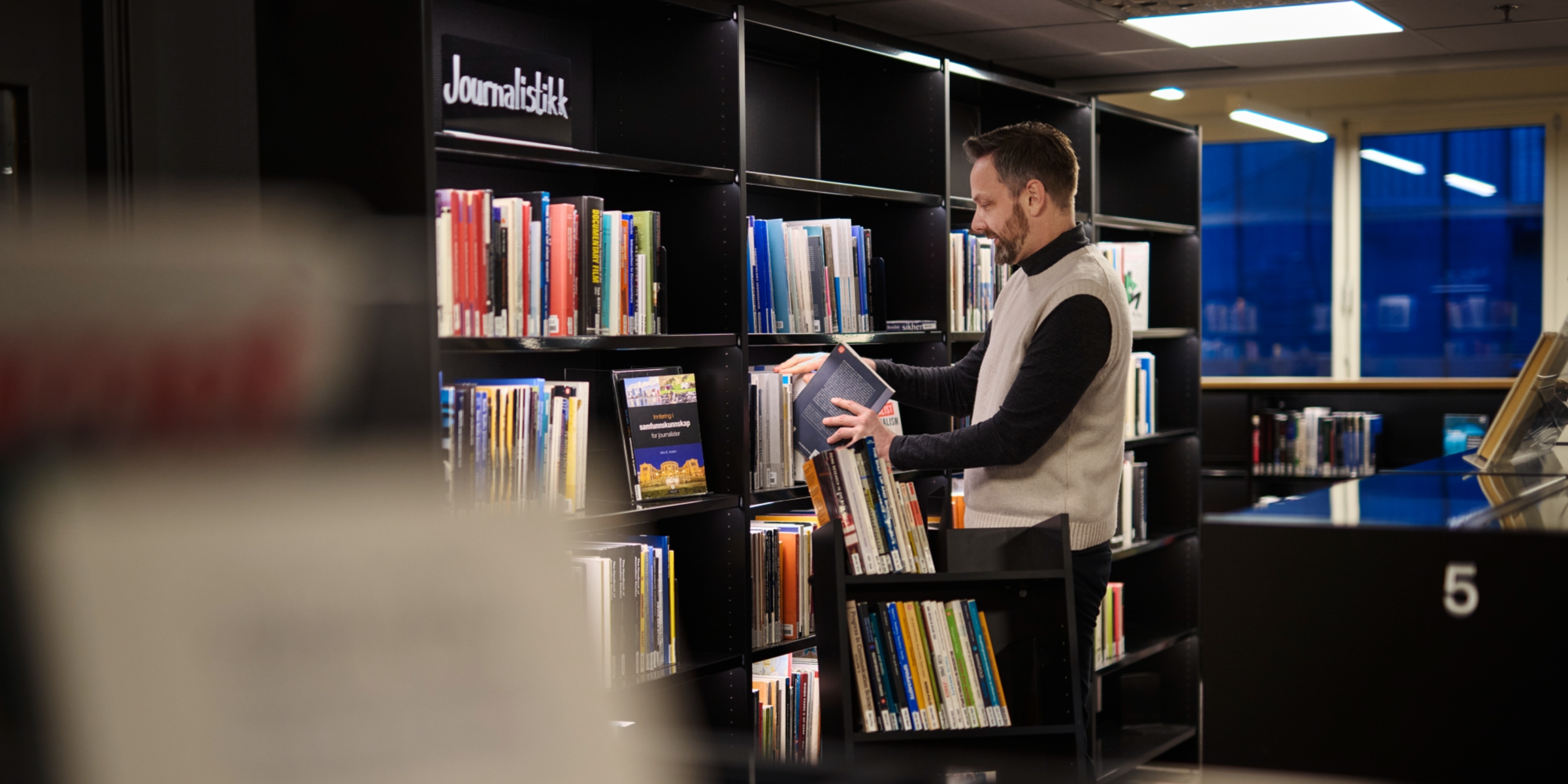 Mann setter bøker på plass i et bibliotek