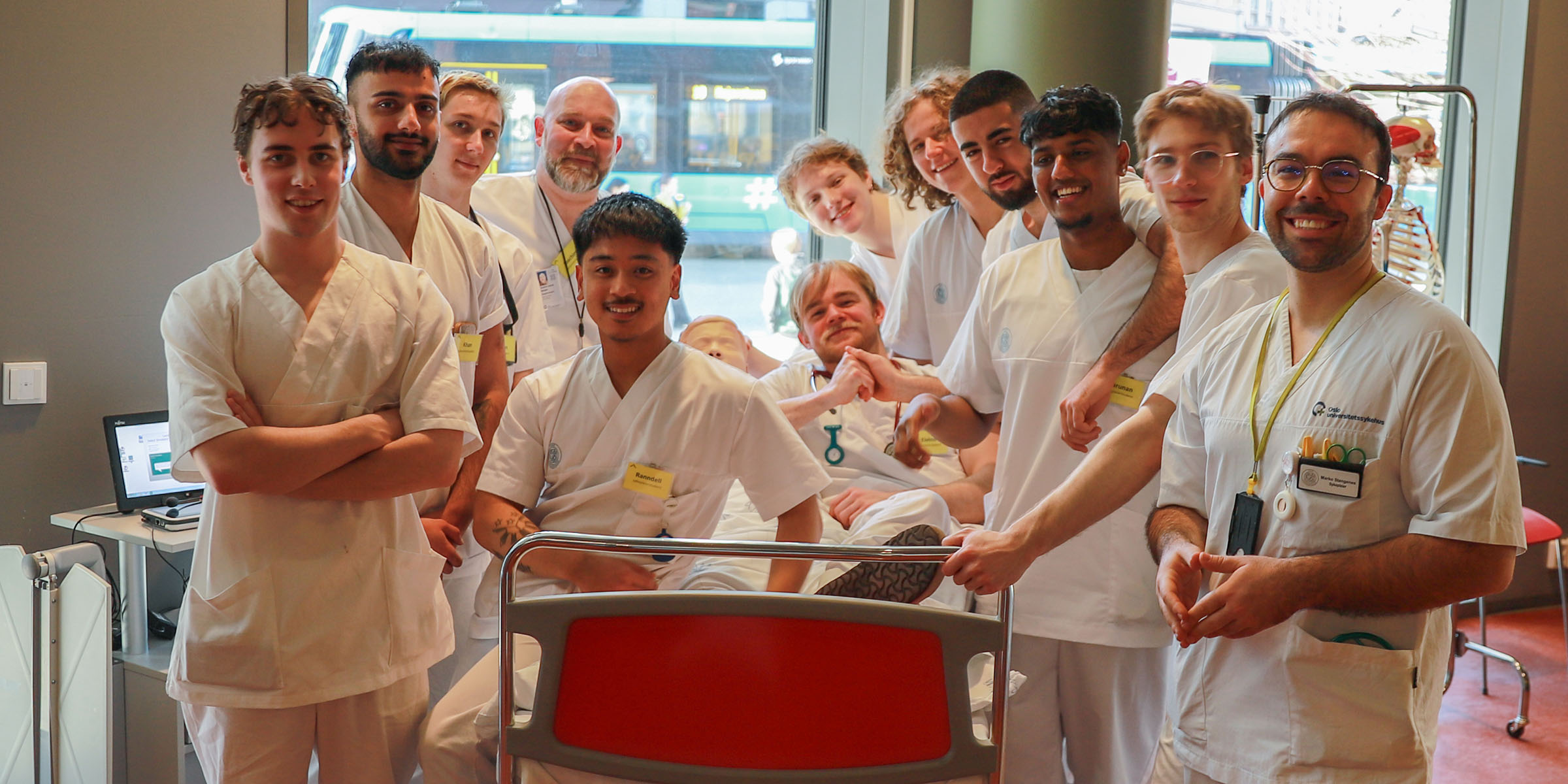 En gruppe menn i sykepleieruniform står vendt mot kamers rundt en sykeseng.