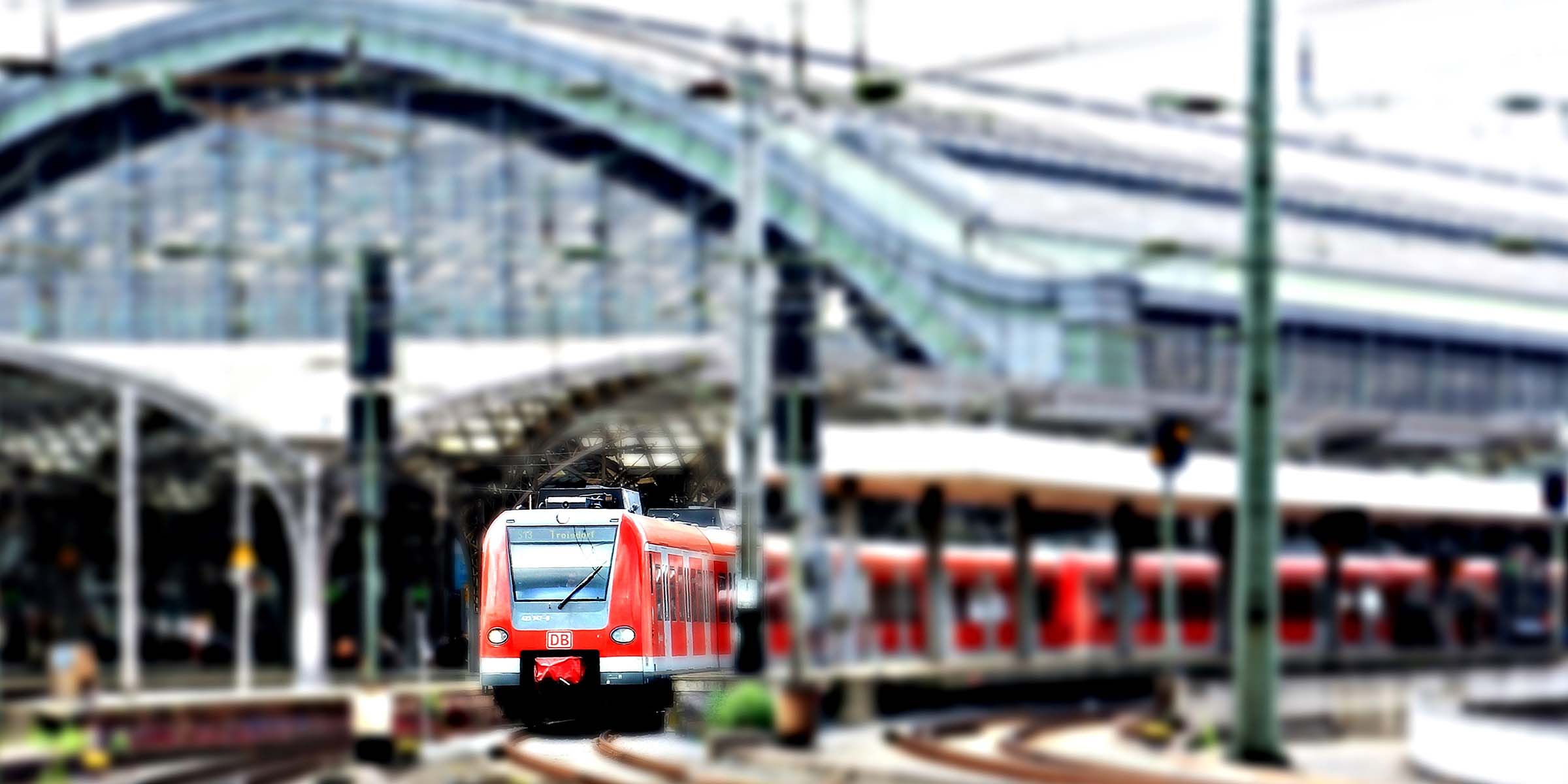 Et rødt og grått tog kjører ut fra jernbanestasjonen i Köln.