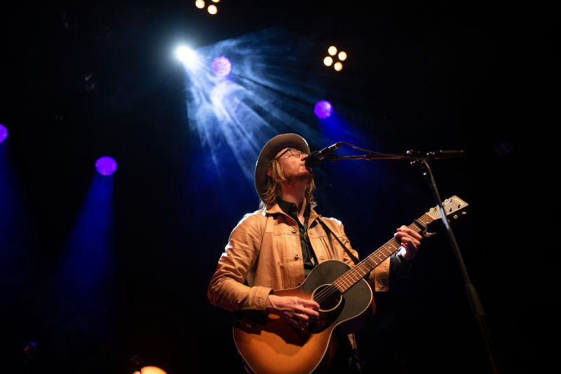 Adam Douglas på en scene som spiller gitar og synger i en mikrofon