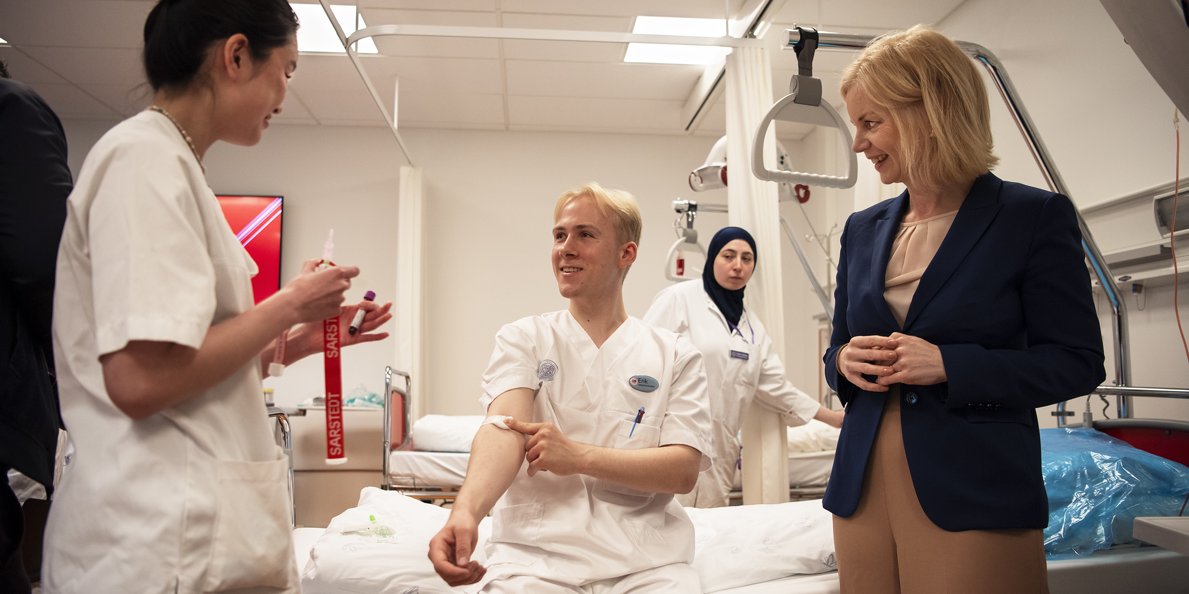 Foto av forsknings- og høyrere utdanningsminister Sigrun Aasland som deltar på blodprøvetakingskurs med studenter på OsloMet.