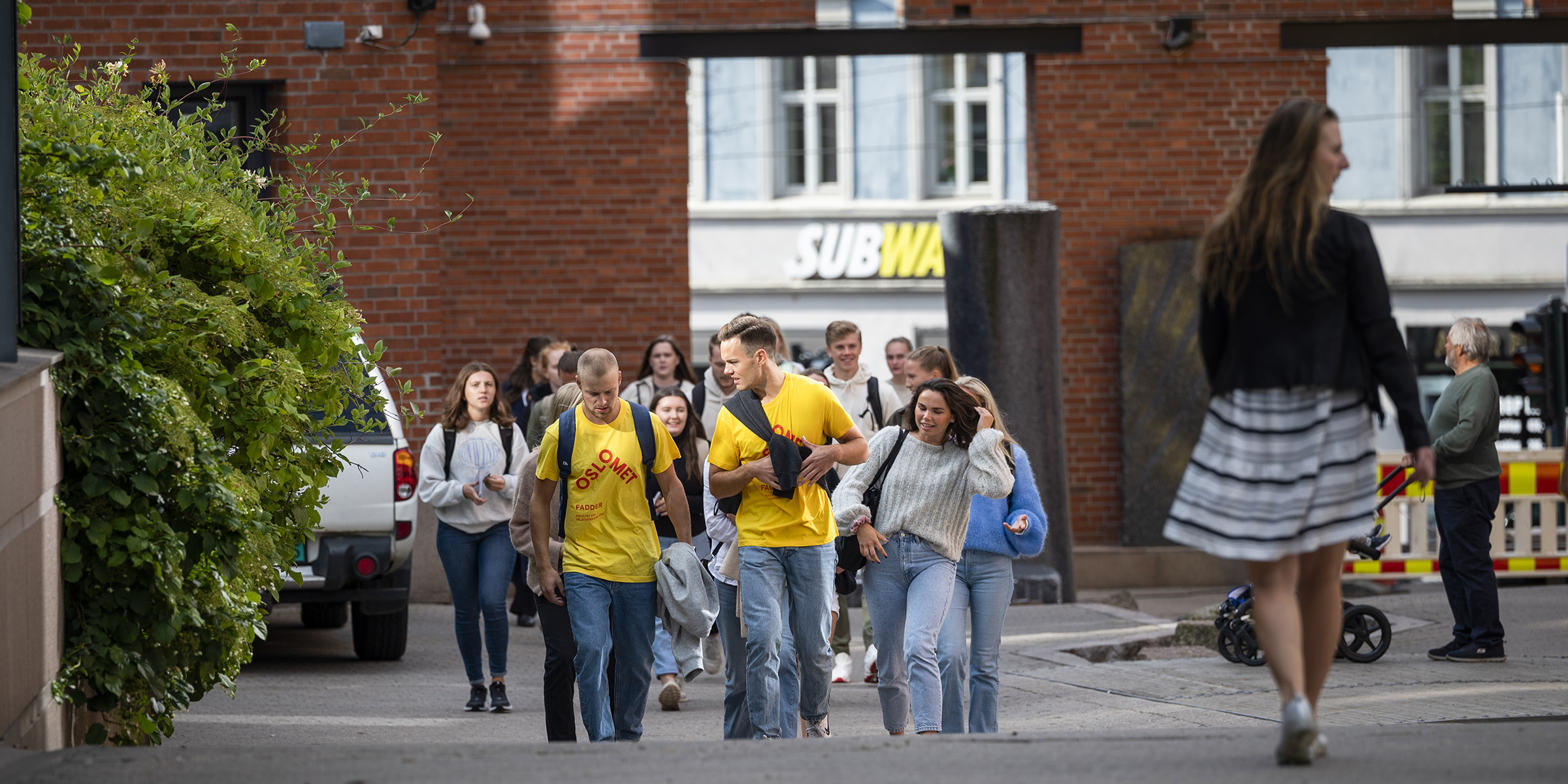 To studenter i fadder-tskjorter går sammen med en gruppe nye studenter gjennom OsloMets campus i Pilestredet.