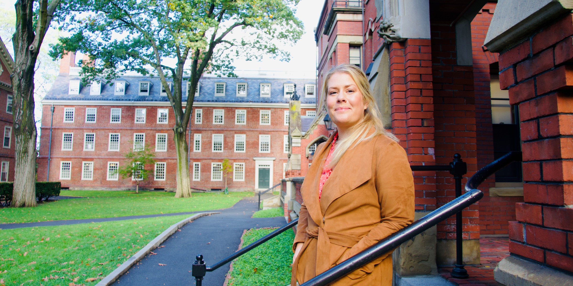 Foto av Miriam Sinkerud Johnson stående på trappen utenfor bygget der hun jobber på Harvard University. Trær og bygg i bakgrunnen.