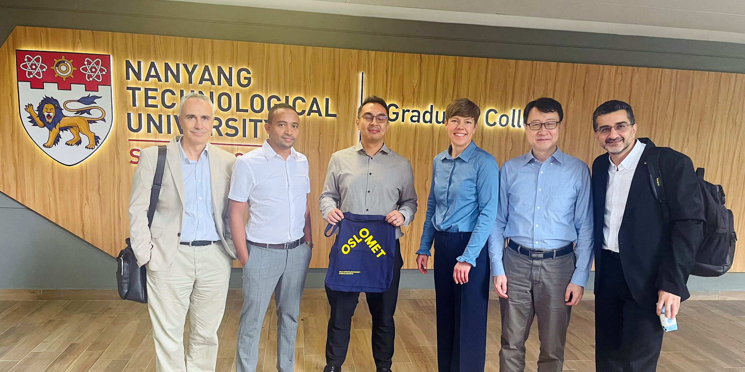 The picture shows Ali Muhtaroglu, Yonas Zewdu Ayele, Imran Halimi Bin Ibrahim, Astrid Oust Janbu, Liu Ming and Peyman Mirtaheri in front of a wall on the university NTU.