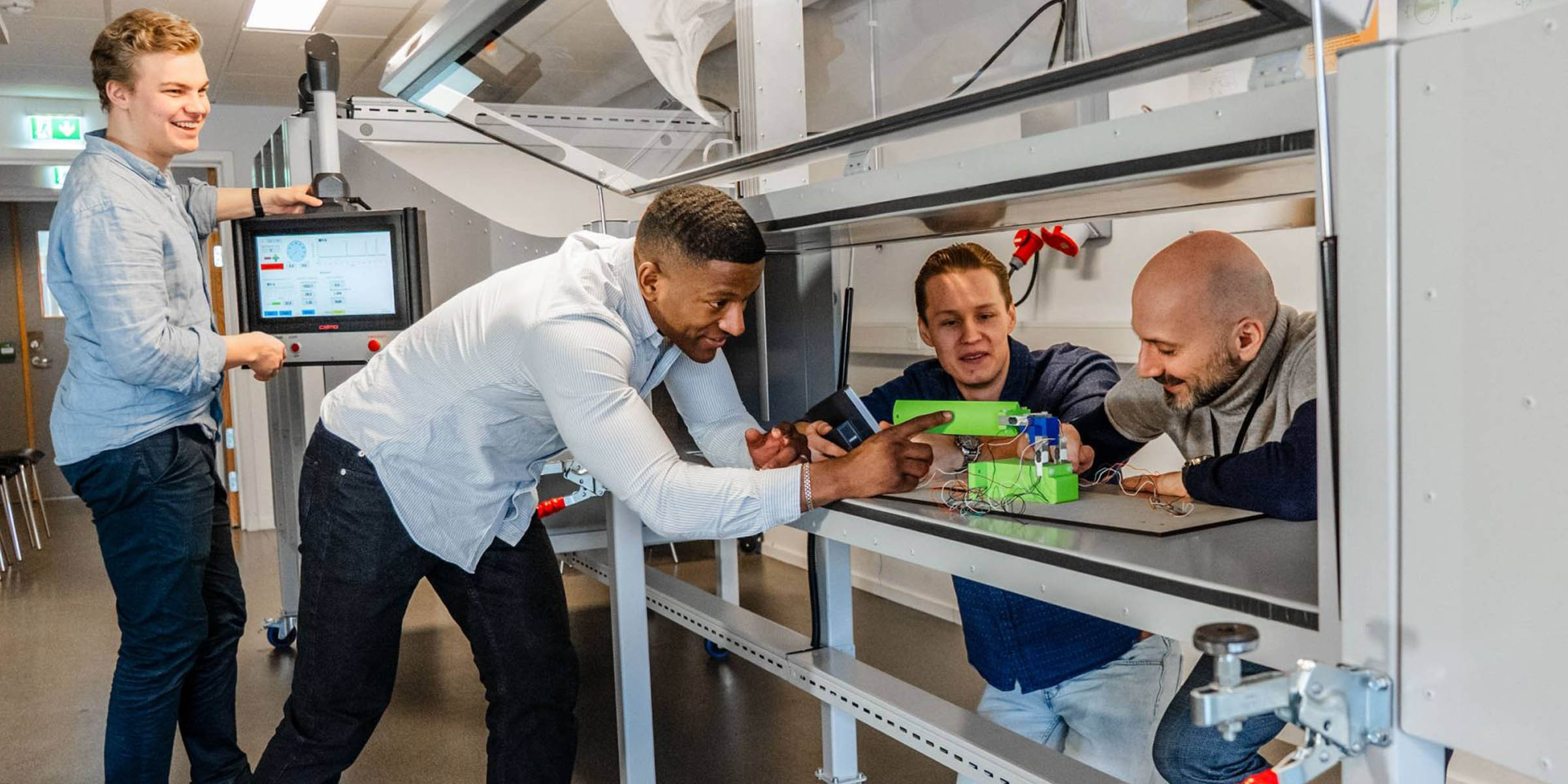 Foto av fire studenter og ansatte som studerer en innretning på den nye grønn energi-laben.