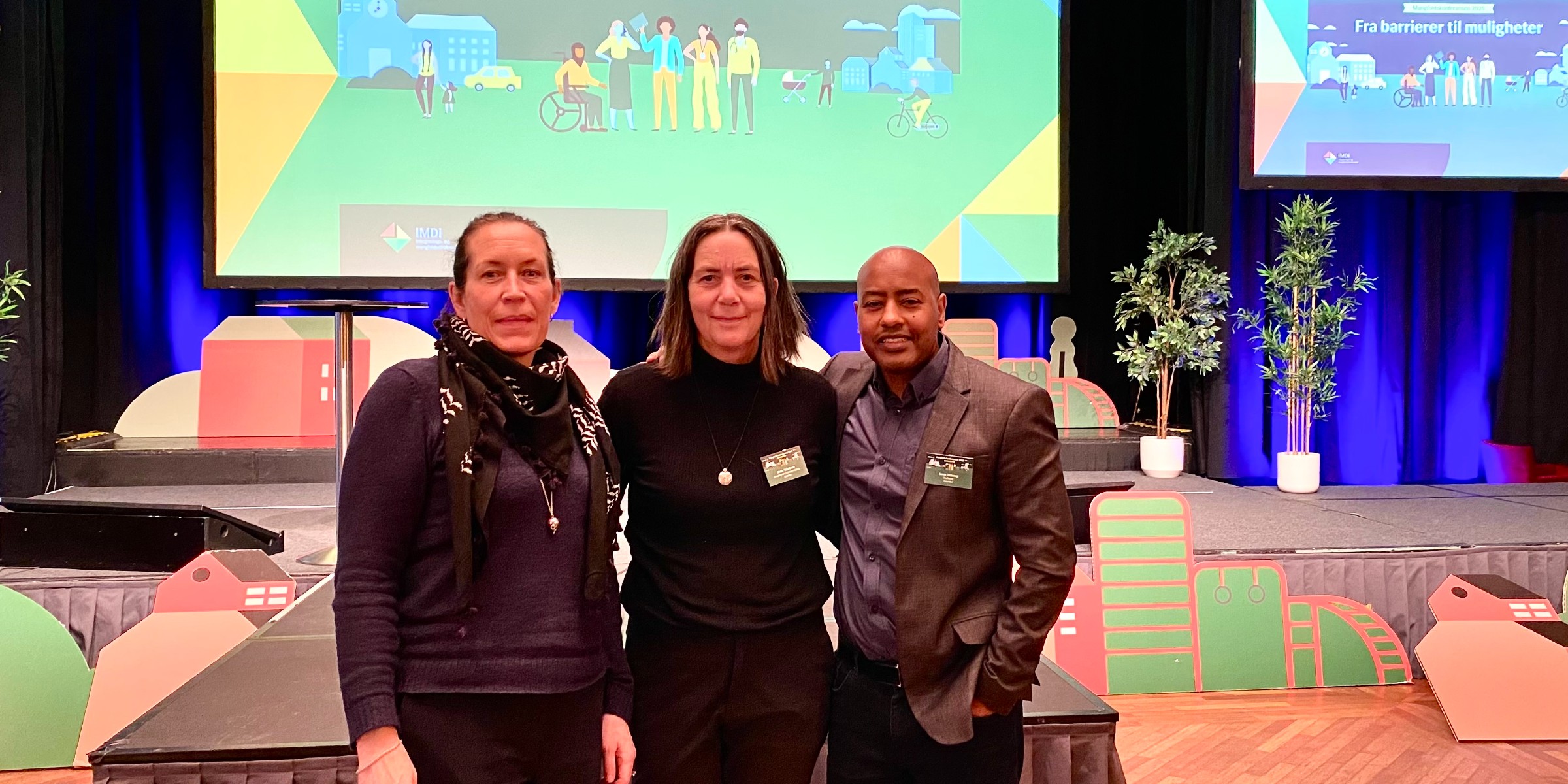 Foto av tre medlemmer av prosjektgruppa stående sammen i en konferansesal med et lerret i bakgrunnen.