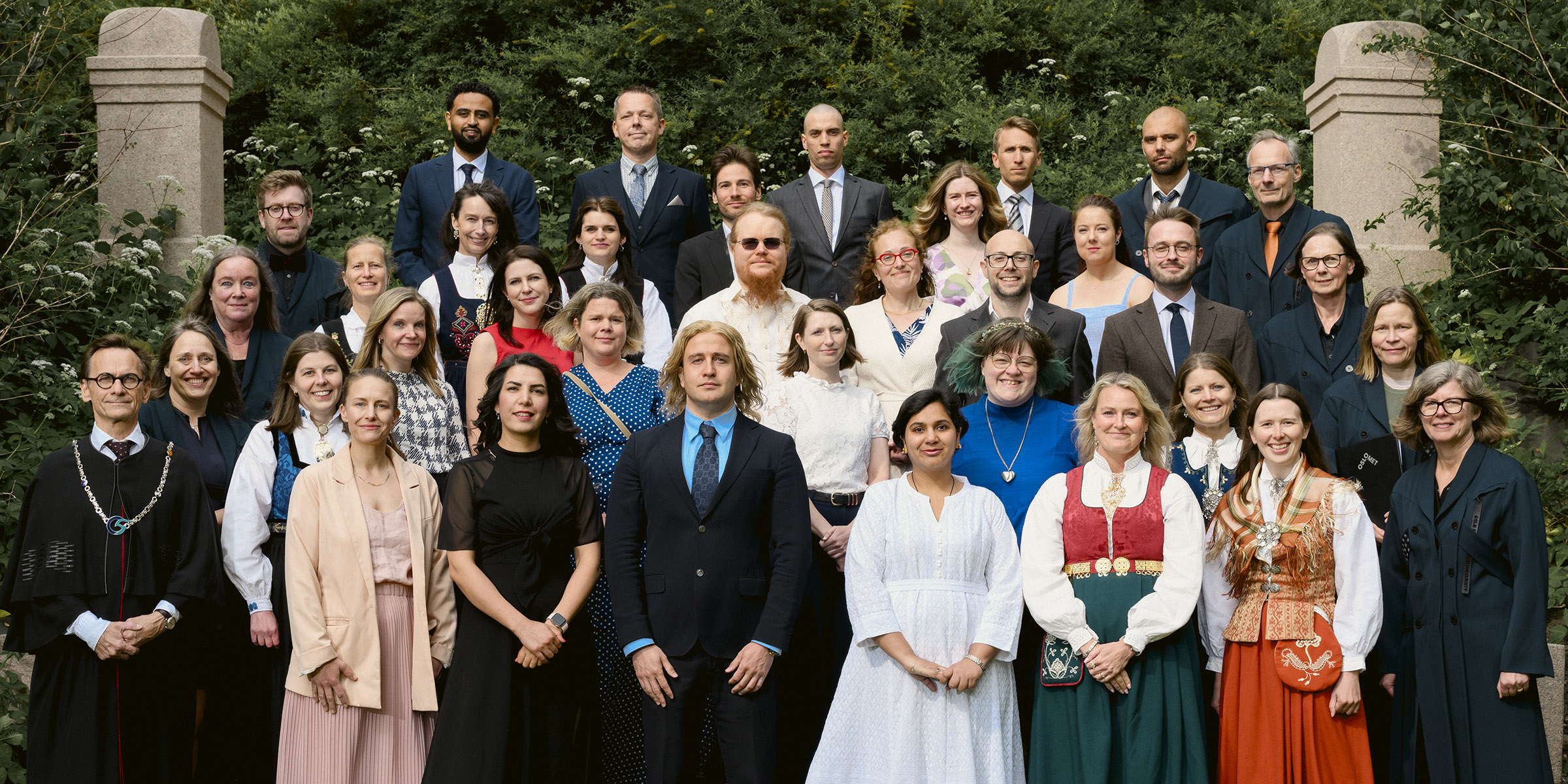 Foto av 27 av de nye doktorene sammen med rektorat og dekaner, står oppstilt i en hage.