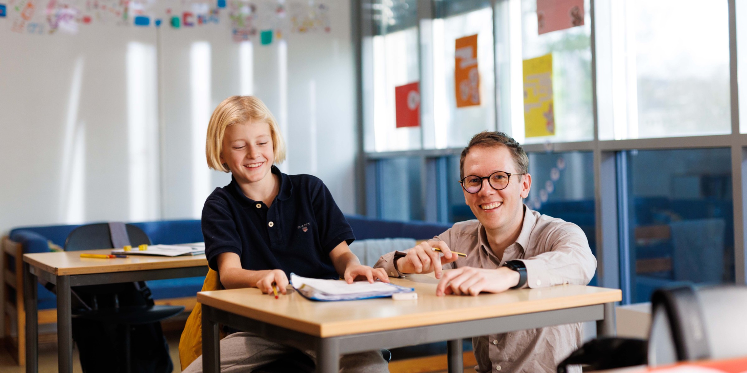 Bildet viser en elev ved skolepulten sammen med en lærer.