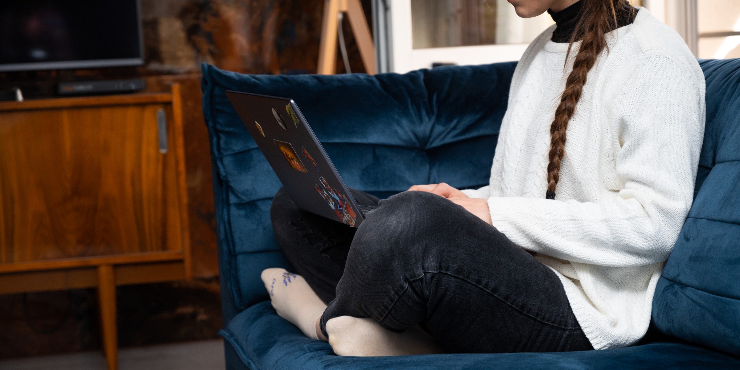 Bilde av en damen som sitter i sofaen med PC-en på fanget.