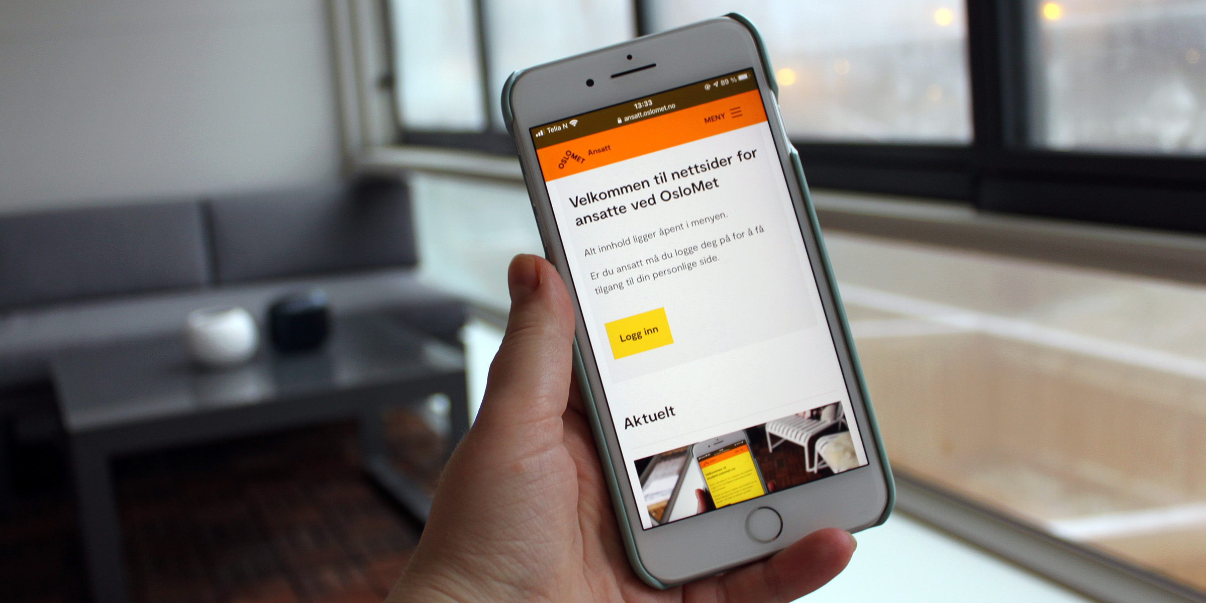 Bilde av hand som held i mobil med ansatt.oslomet.no på skjermen. Sofa i bakgrunnen.