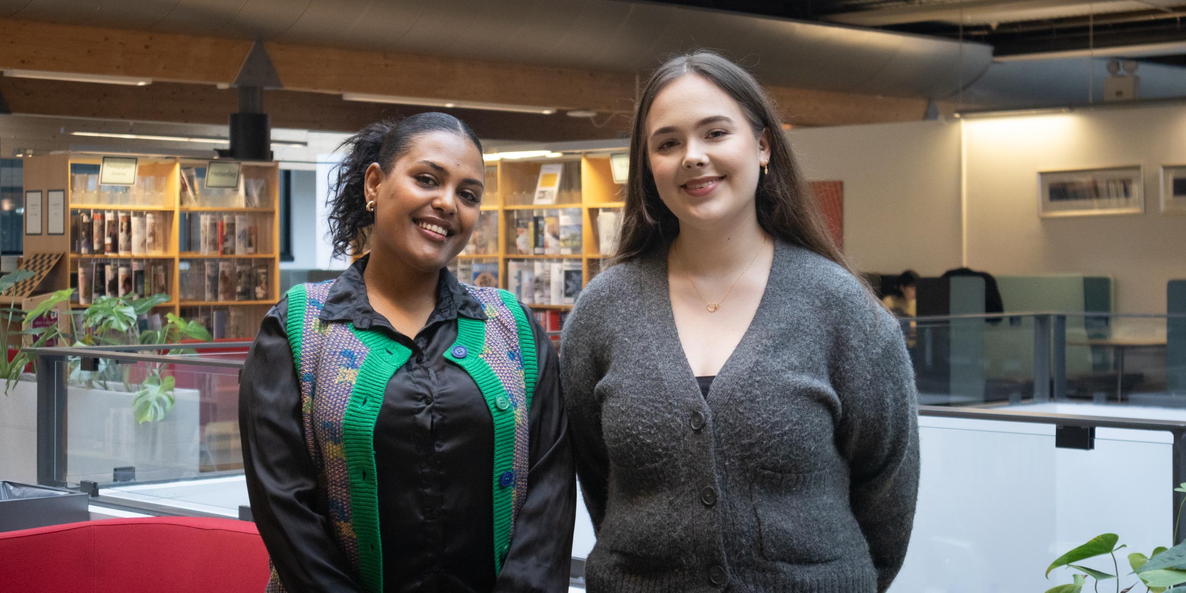To sykepleiestudenter ved OsloMet står i universitetsbiblioteket og smiler til kamera.