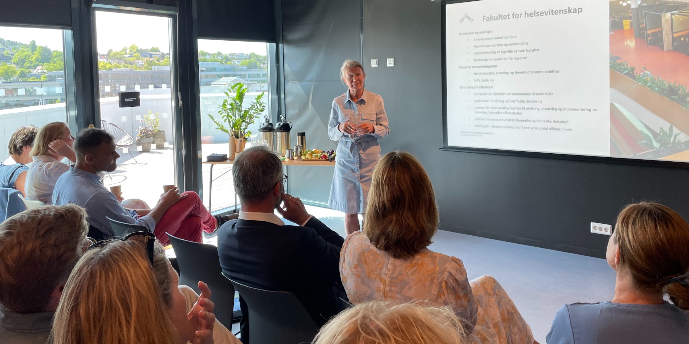 Foto av dekan ved OsloMet sitt fakultet for helsevitenskap, Gro Jamtvedt, som holder en presentasjon i et møterom med utsikt til Lillestrøm fra vinduet bak.