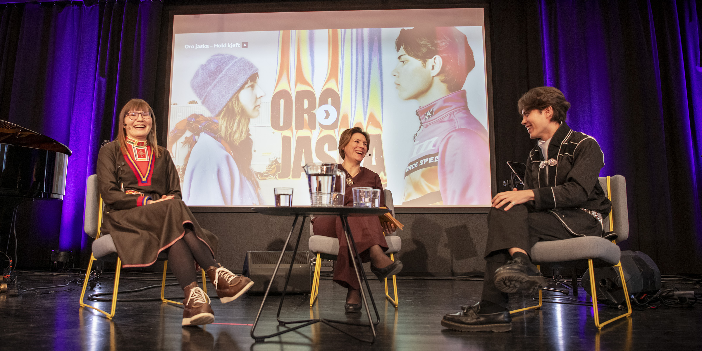 Tre mennesker i samtale på en scene.