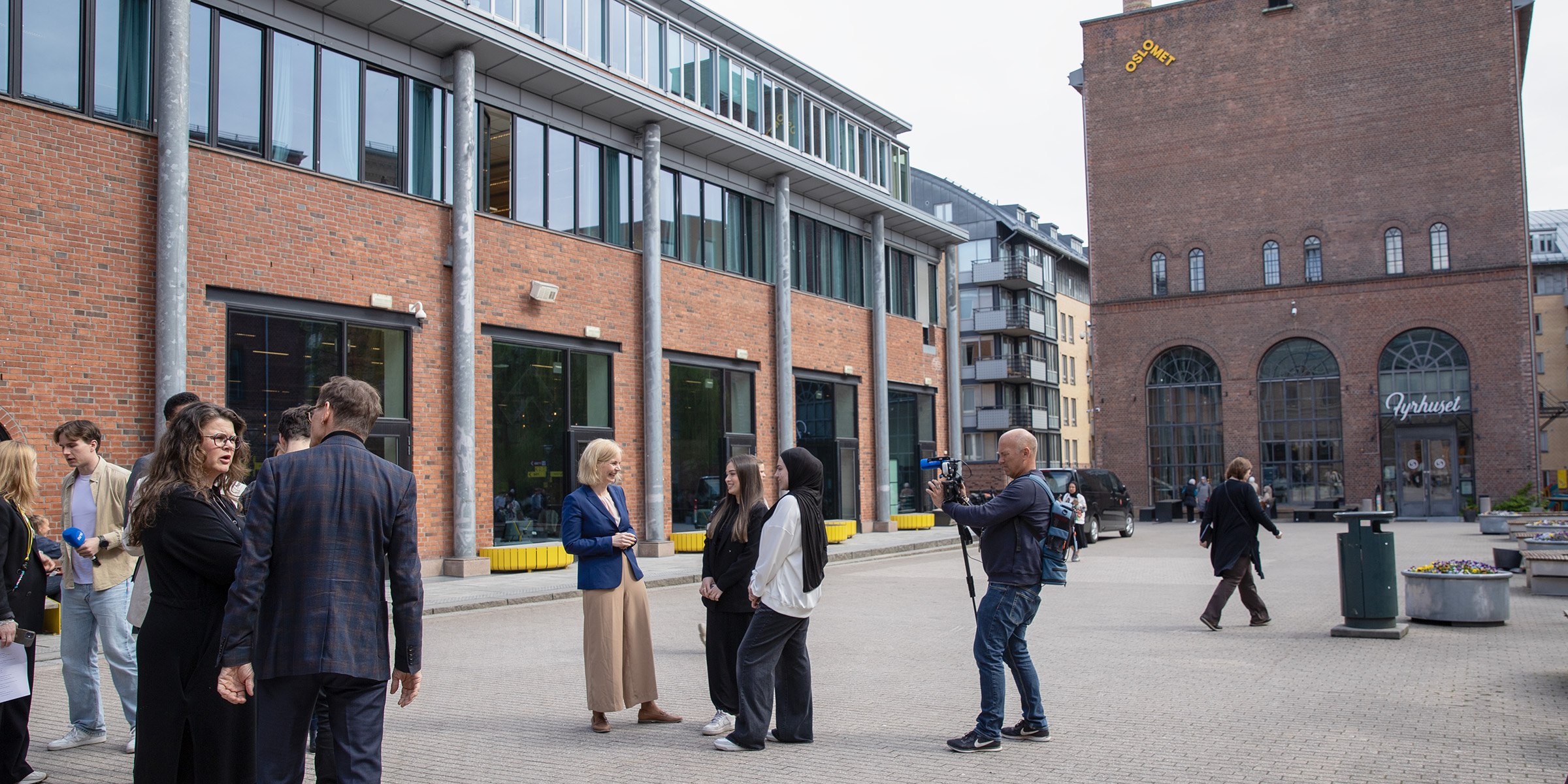 Foto av statsråd Aasland som snakker med to unge søkere ute på campus, med NRK-fotograf som filmer dem.