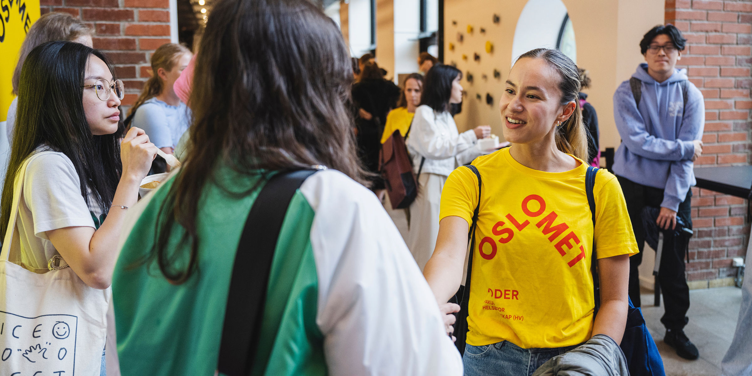 OsloMet buddy in a yellow t-shirt saying hello to new students at campus.