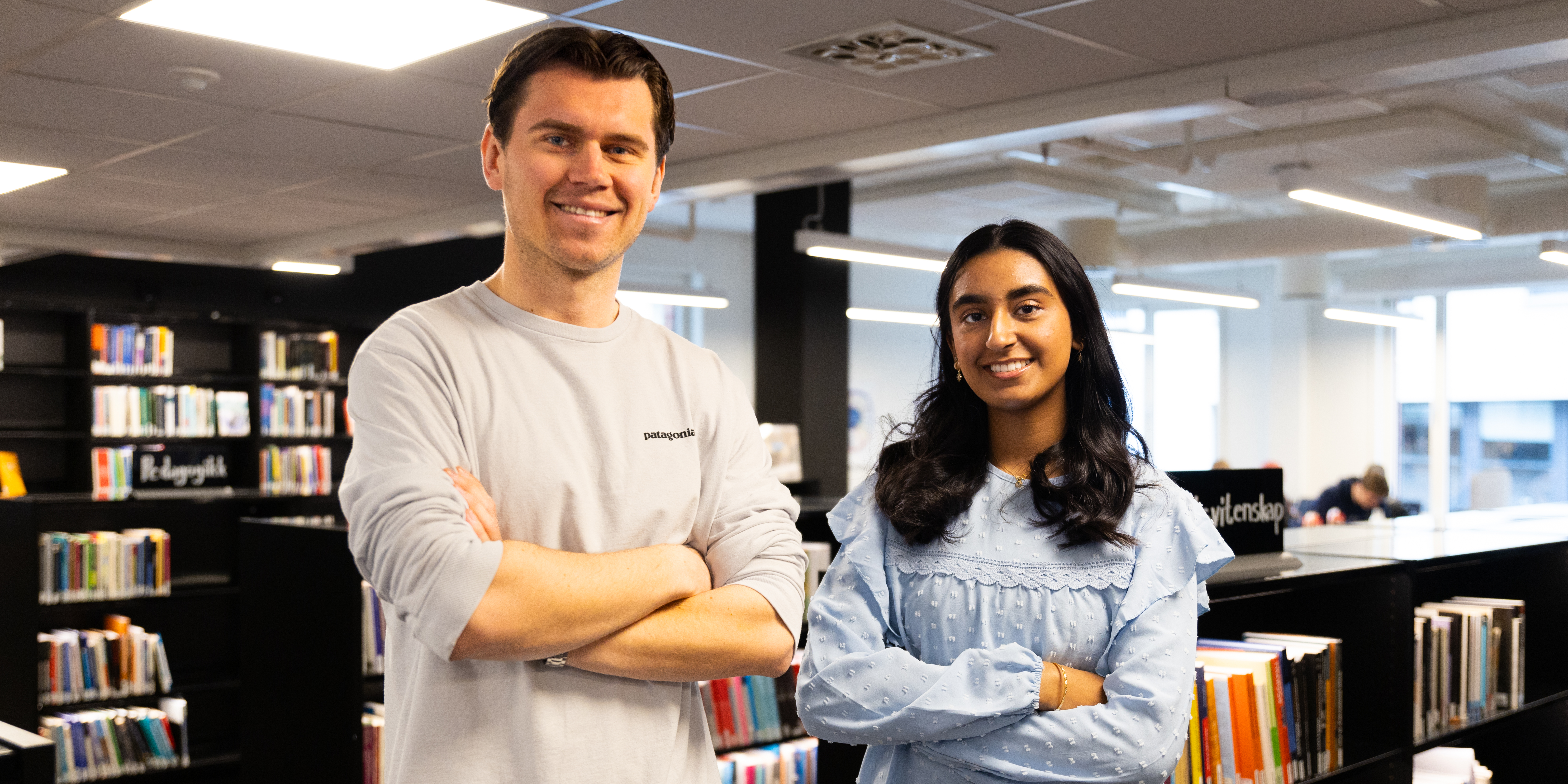 Economics and Administration students Sander and Alina stand in the library at OsloMet and smile at the camera.