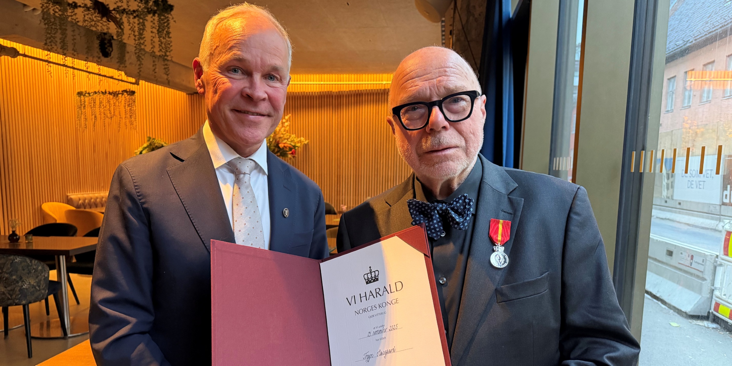 Jan Tore Sanner og Trygve Aasgaard holder diplom som viser at Aasgaard mottar Kongens fortjenstmedalje.