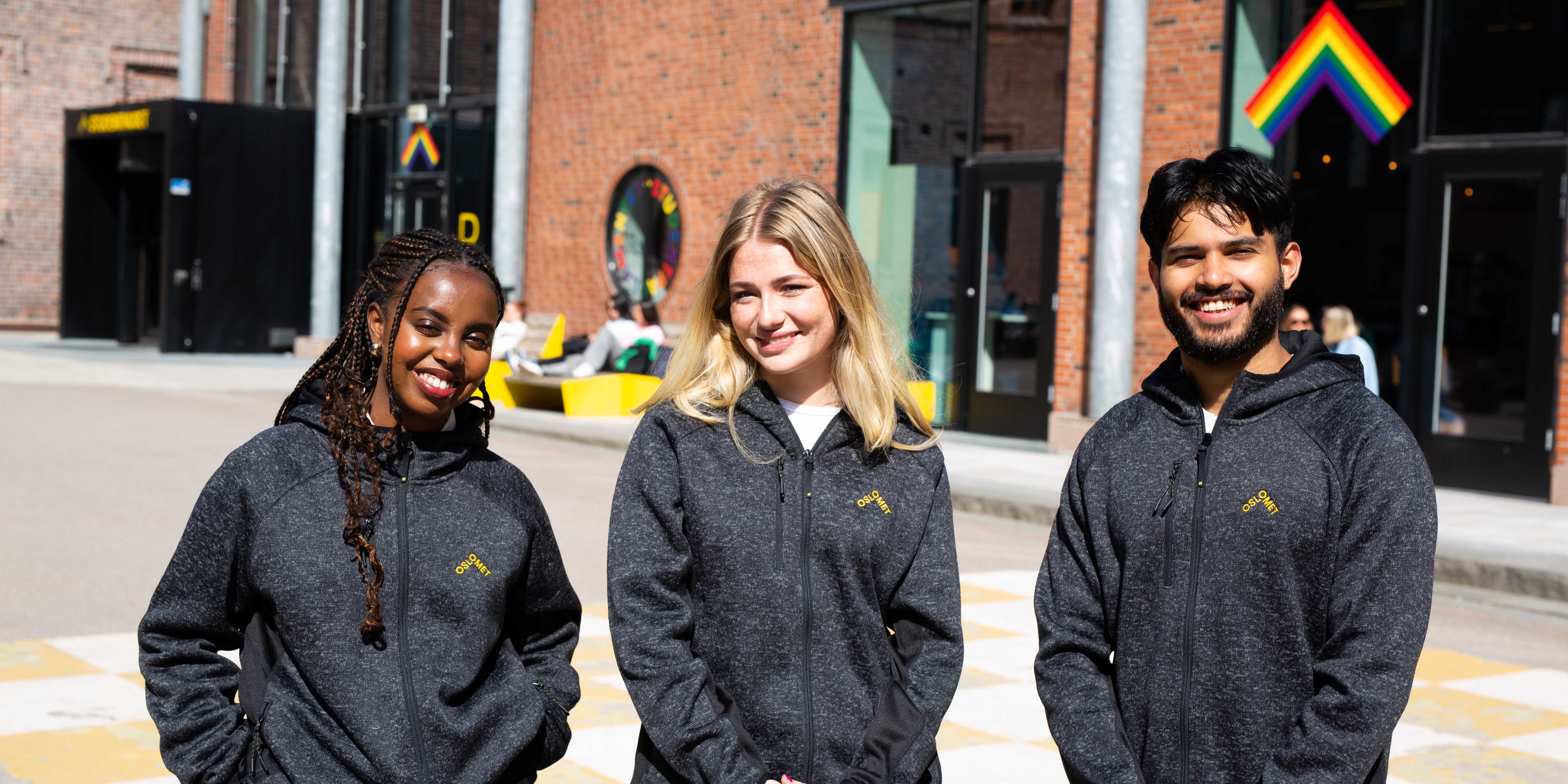 Three student wearing grey mottled fleece jackets. The jackets have a yellow OsloMet logo in front on the left side
